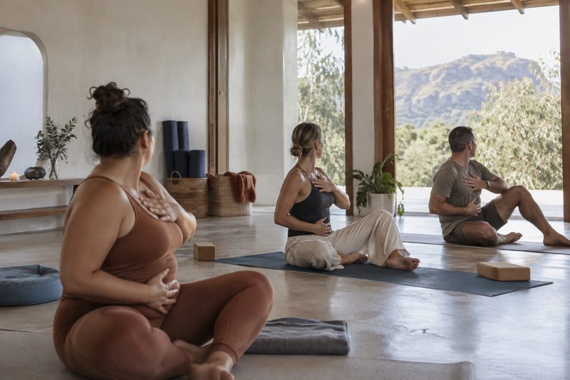 Three adults practise guided breathing and mobility in a light studio